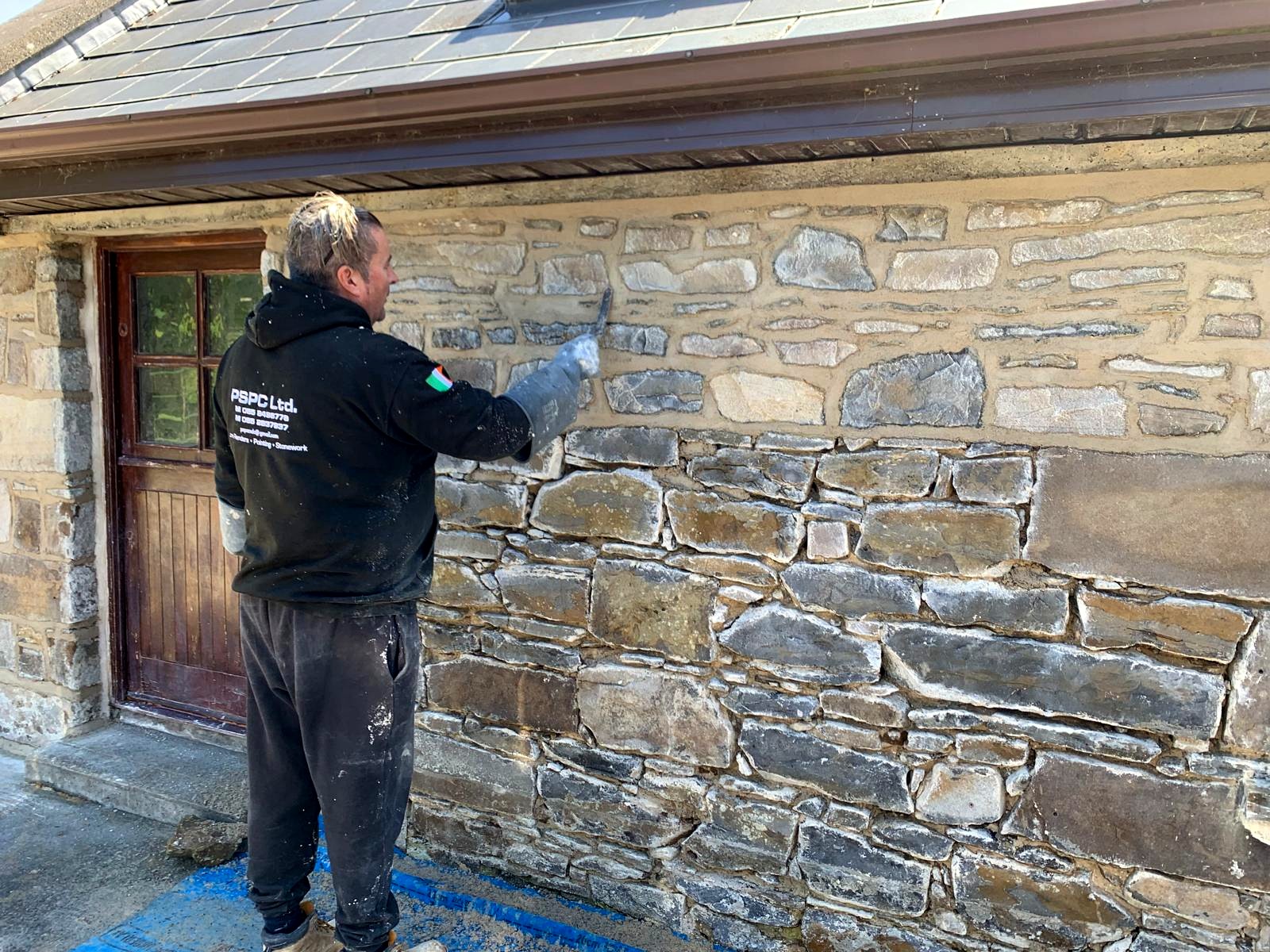 Phoenix Stone craftsman lime pointing a traditional stone cottage beside its timber door