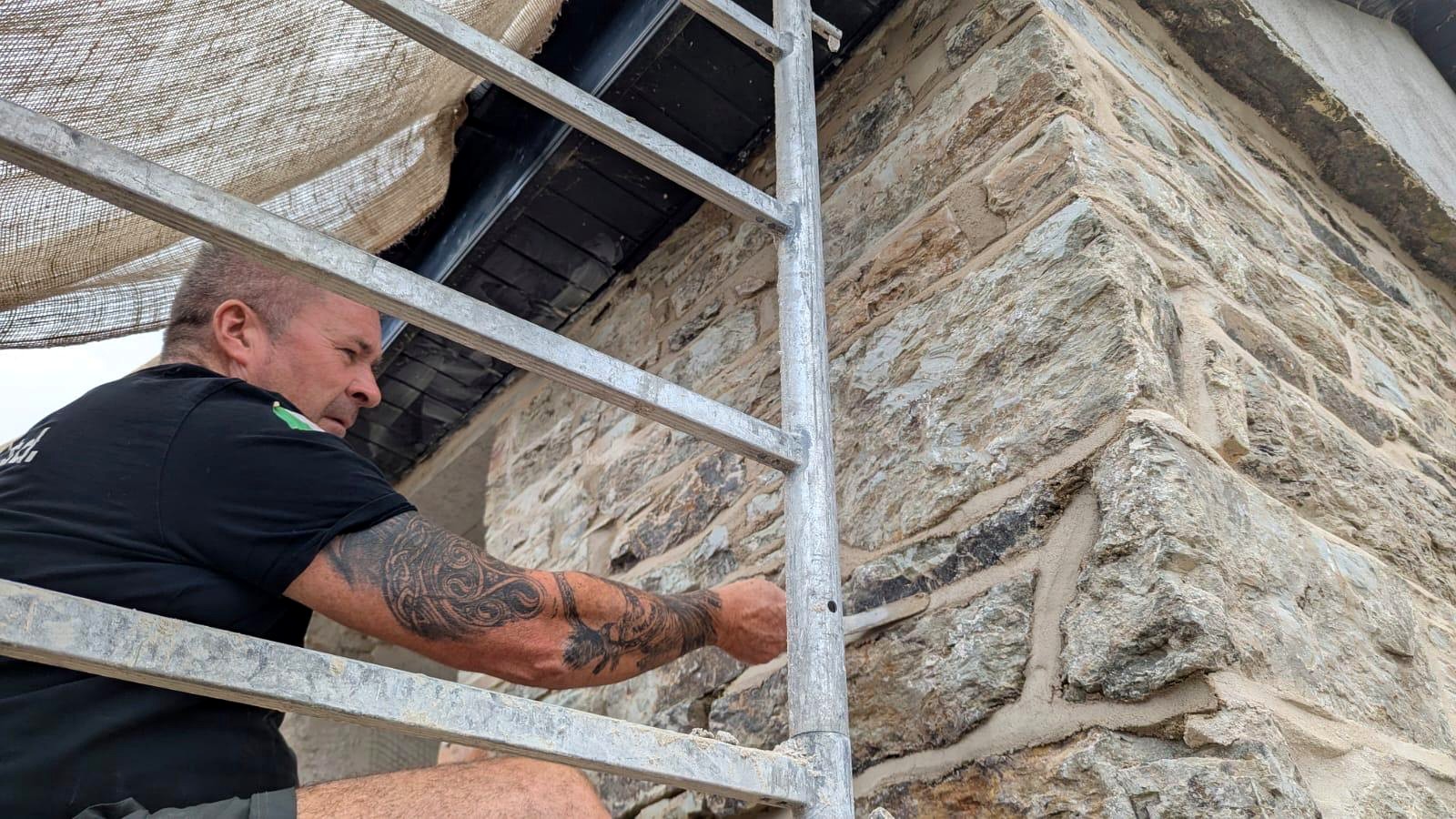 Craftsman lime pointing stone quoins from scaffolding under the eaves