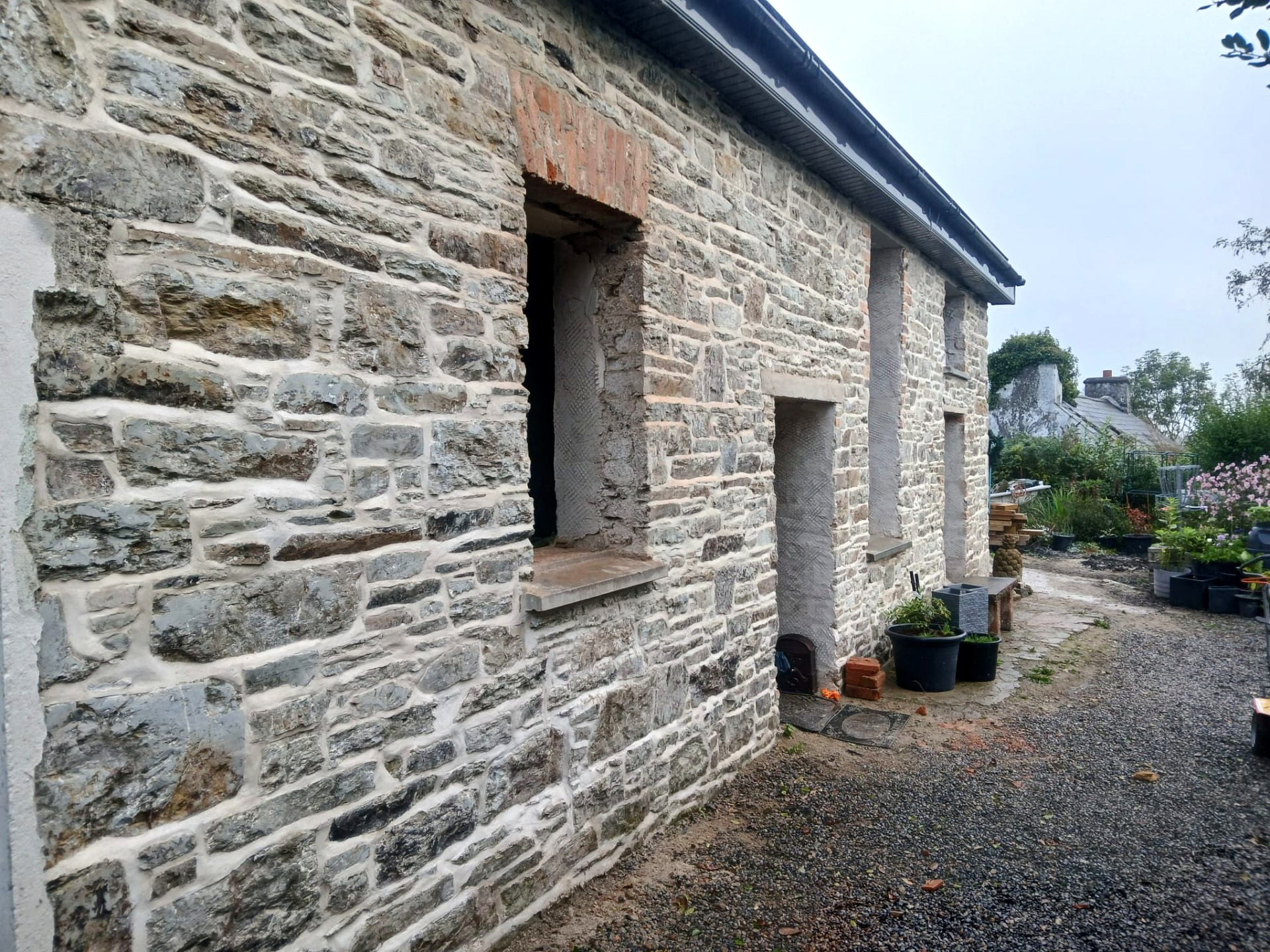 Side elevation of a lime pointed stone outbuilding with brick-dressed window reveals