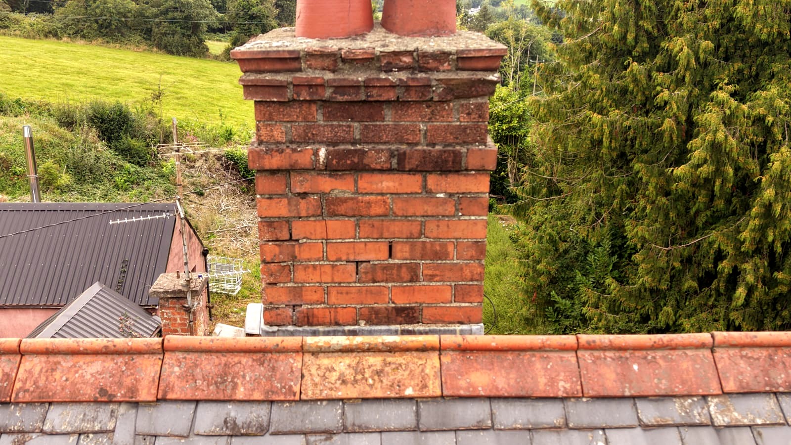 Drone view along the ridge tiles to a brick chimney stack