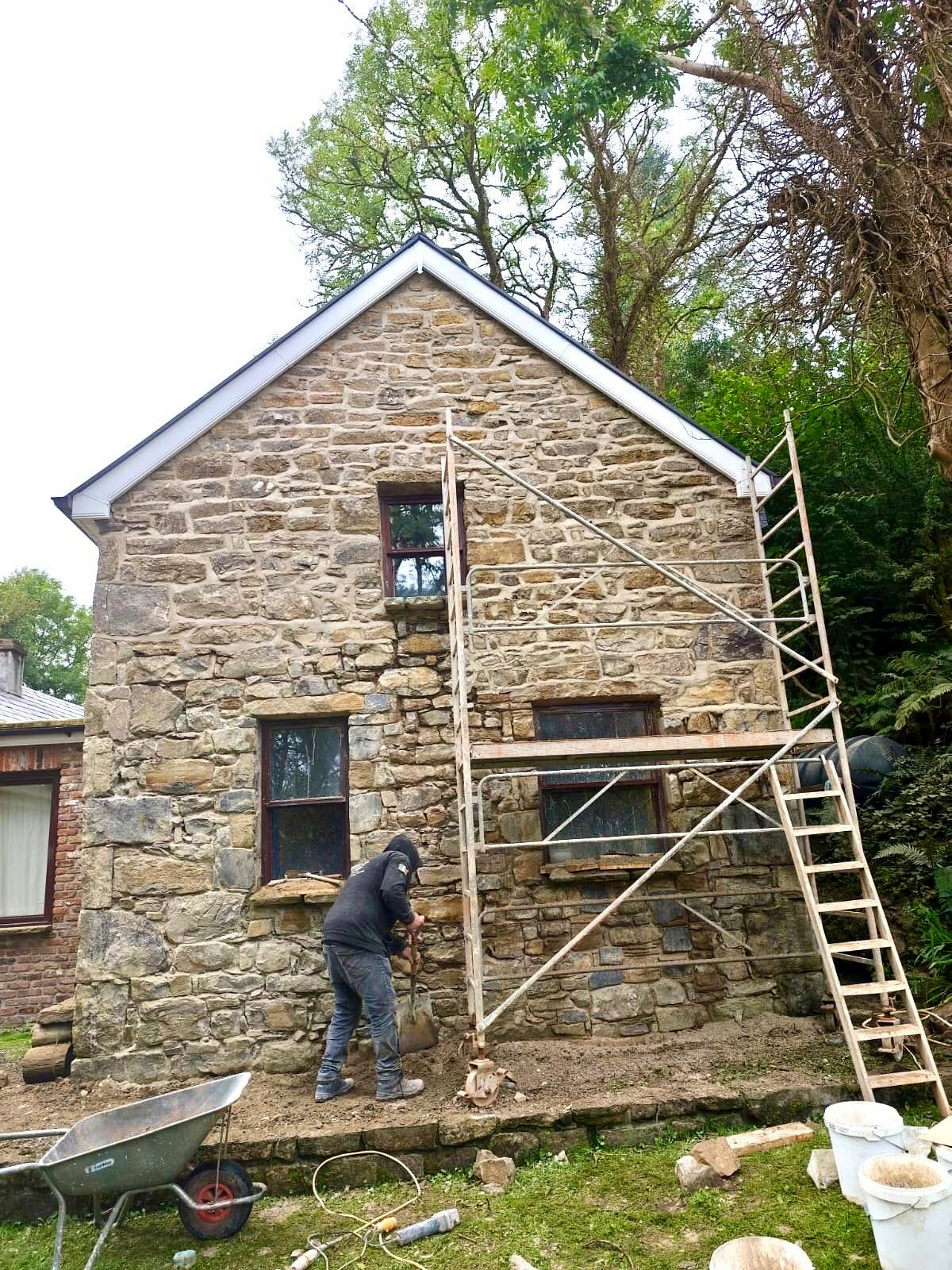 Craftsman repointing a tall rubble stone gable with scaffold and ladder in place