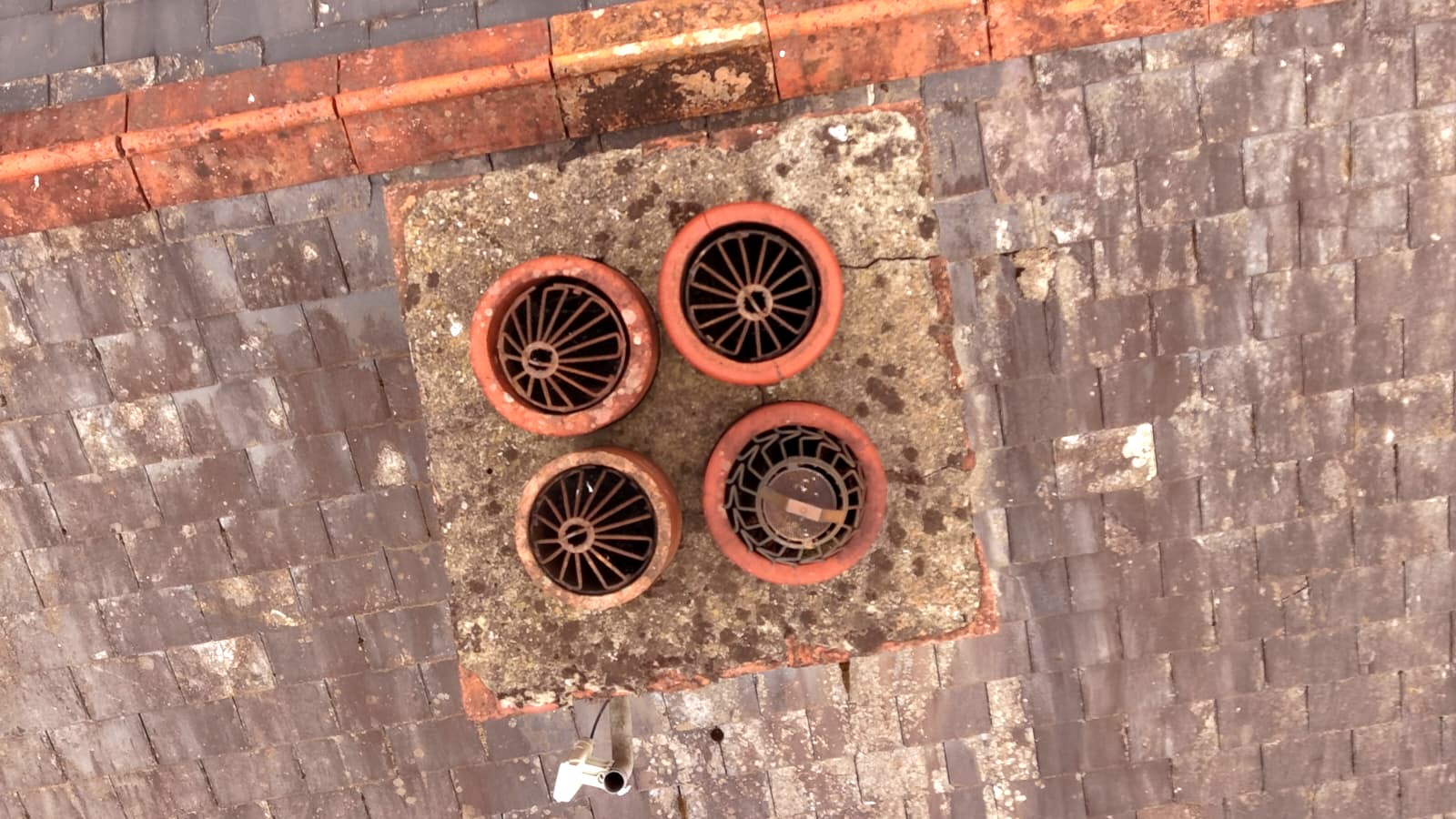 Second chimney crown from above, weathered and stained, with lichen on surrounding slates